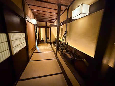 Corridoio interno del ristorante a Kurochaya con pavimento in tatami, pareti ocra e decorazioni in legno illuminate.