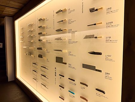Una parete retroilluminata con esposizione coltelli a Jikko ad Osaka, mostrando vari modelli e materiali dei manici.