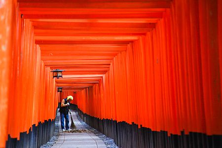 Una persona cammina sotto i torii rossi del Fushimi Inari a Kyoto.