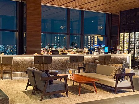 La lobby a Mitsui Garden Hotel Toyosu Premier con divani, poltrone e bancone bar davanti a grandi vetrate panoramiche.
