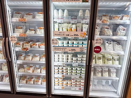 Tre ante vetrate di frigoriferi in un negozio Muji a Tokyo contenenti gelati e prodotti alimentari confezionati.