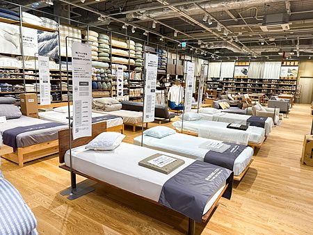 L'interno del negozio Muji a Tokyo mostra file di letti ordinati in esposizione con scaffali pieni di prodotti tessili.