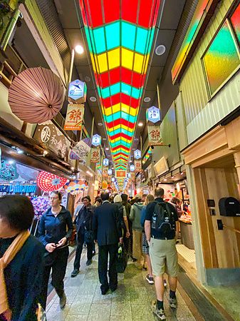 Persone camminano nel mercato coperto del Nishiki Market di Kyoto, con luci colorate sul soffitto.
