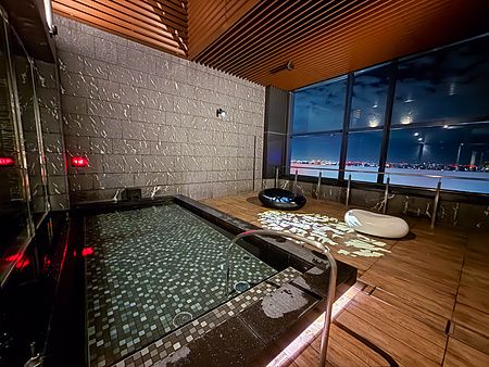 Veduta notturna dell'onsen pubblico con vista al Mitsui Garden Hotel Toyosu Premier, con vetrate panoramiche.