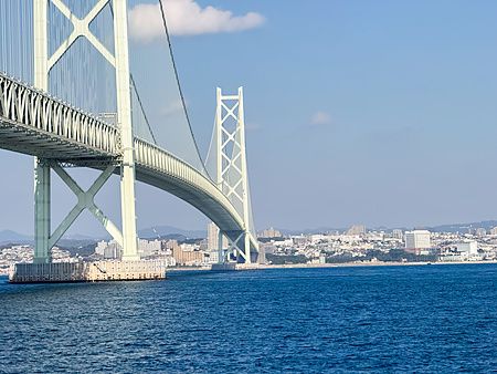 Il Ponte dello stretto di Akashi si estende sopra il mare blu con le sue torri bianche visibili dal basso.