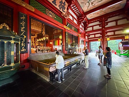 Visitatori in preghiera all'interno del tempio Senso-ji ad Asakusa, caratterizzato da strutture in legno rosso.