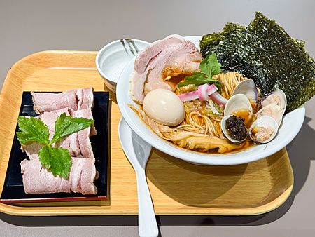 Una ciotola di ramen con vongole e carne servita su un vassoio di legno presso il ristorante Mugi to Olive a Tokyo.