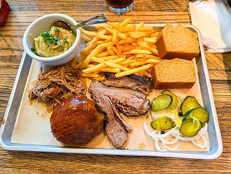 Vassoio di metallo con brisket, carne sfilacciata, patatine, purè e pane di mais servito al ristorante Smokehouse.