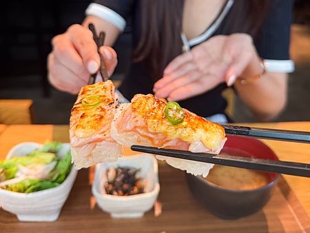 Sushi aburicious tenuto con bacchette al Kinka Sushi Bar Izakaya.