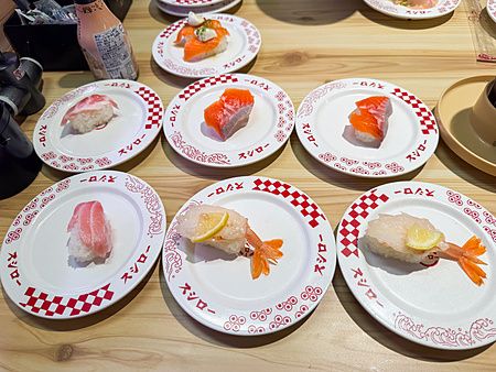 Piatti di nigiri sushi marchiati Sushiro disposti su un tavolo di legno in un ristorante.