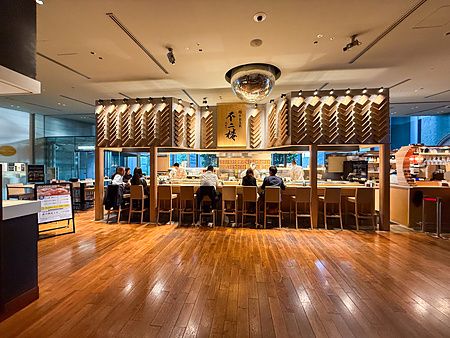 Interno del Sushi & Bar Fujiro Marunouchi Tokyo con bancone in legno e persone sedute a mangiare nel Marunouchi Building.