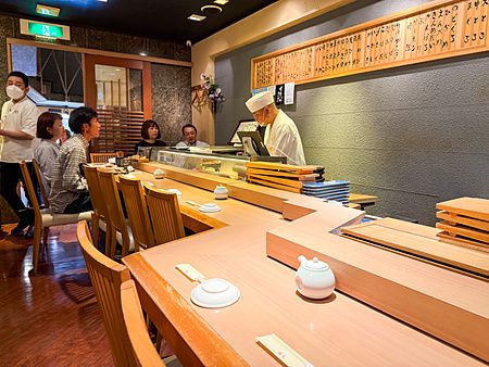 Interno del ristorante Sushimaru a Shinjuku con un sushi chef dietro il bancone e alcuni clienti seduti.