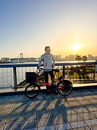 Uomo con bicicletta davanti al tramonto e al Rainbow Bridge ad Odaiba.