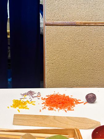 Una sessione di preparazione wagashi a Tsuruya Yoshinobu con ingredienti colorati disposti su un piano di lavoro bianco.