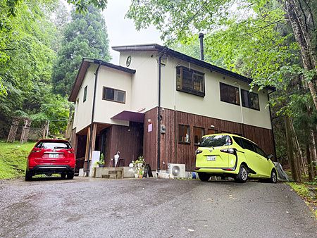 Esterno a VeganLife SoiSoi, un ristorante immerso nel verde con due auto parcheggiate nel piazzale di fronte.