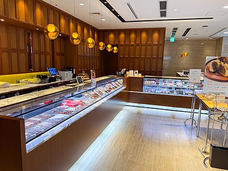 Interno a Wako Tea Salon a Ginza con bancone in vetro, pareti in legno e lampade a sospensione sferiche ambrate.
