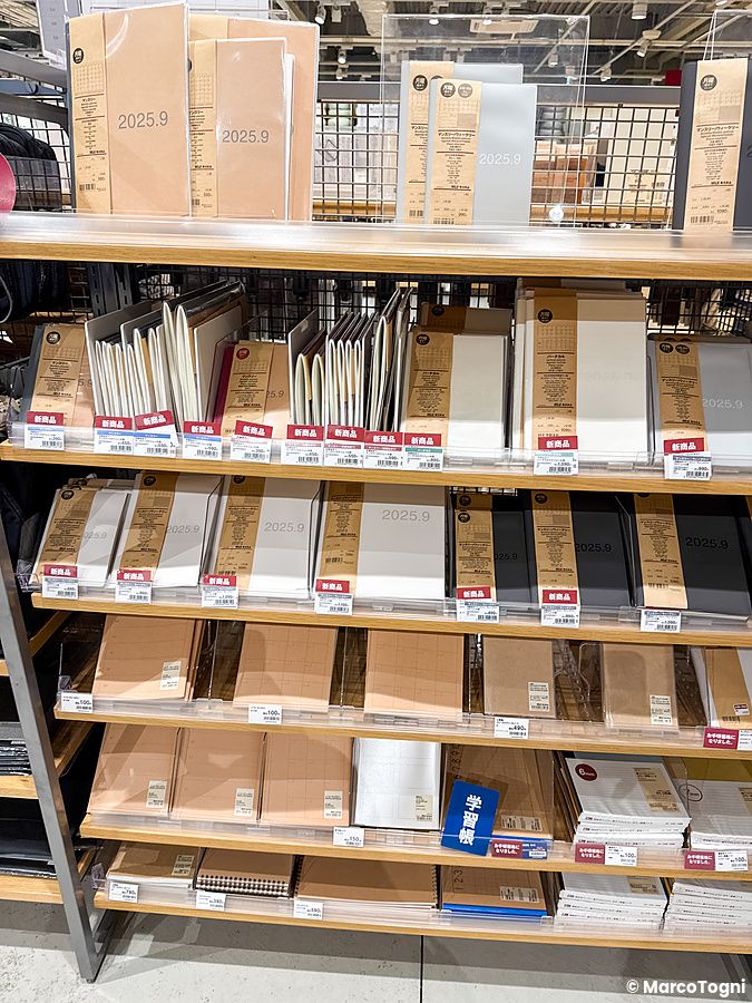 Scaffali di legno in un negozio Muji a Tokyo, pieni di agende e quaderni in carta riciclata con etichette di prezzo.