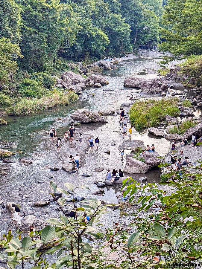 Veduta di persone che camminano nel letto di un torrente roccioso vicino al ristorante a Kurochaya ad Akiruno, Tokyo.