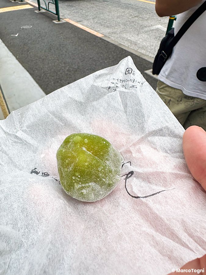 Una mano tiene Aoume, dolce iconico di Kikuzuki, appoggiato sulla sua carta di incarto bianca a Yanaka, Tokyo.
