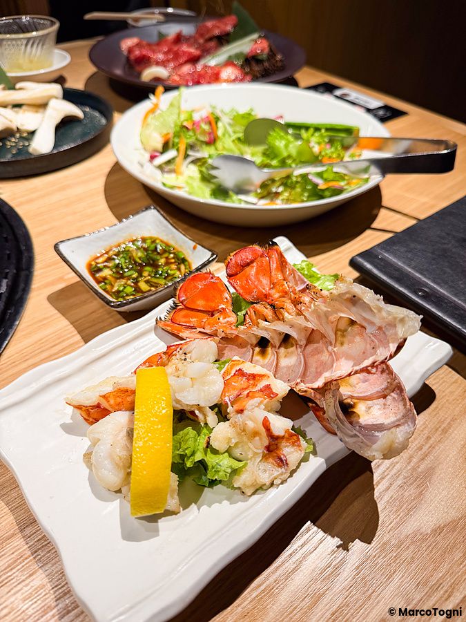 Piatti di aragosta grigliata e insalata serviti su un tavolo di legno al Ristorante Toraji.
