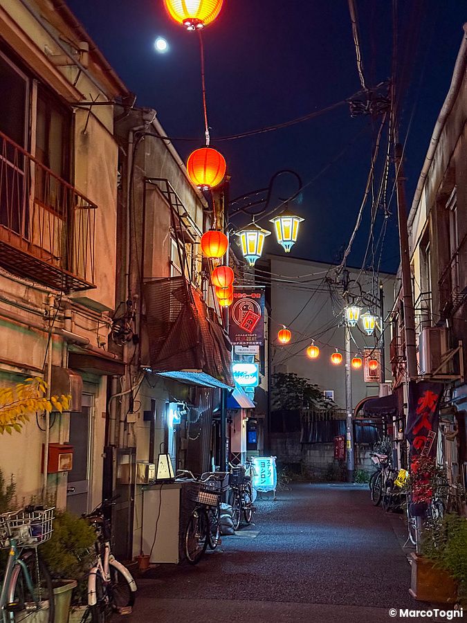 Vicolo notturno ad Asagaya con lanterne rosse sospese e biciclette parcheggiate lungo le pareti degli edifici.