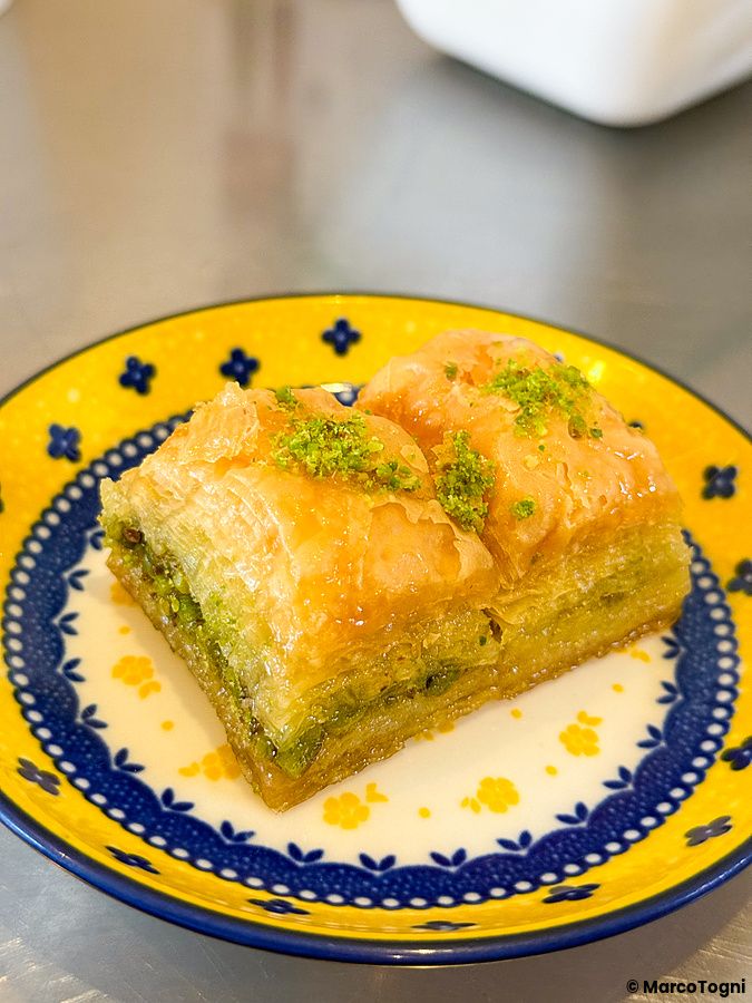 Un piatto con decorazioni blu e gialle su cui sono adagiati due pezzi di baklava al Falafel Sababa.
