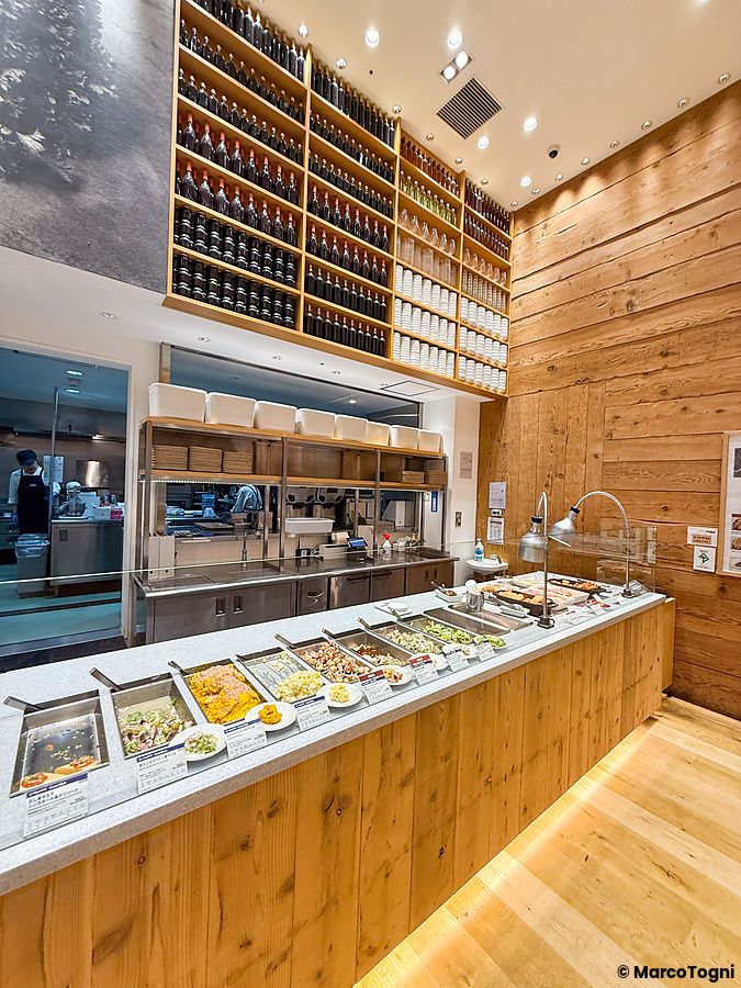 Bancone per scegliere i piatti al Cafe＆Meal Muji di Shinjuku con diverse pietanze in vaschette d'acciaio.