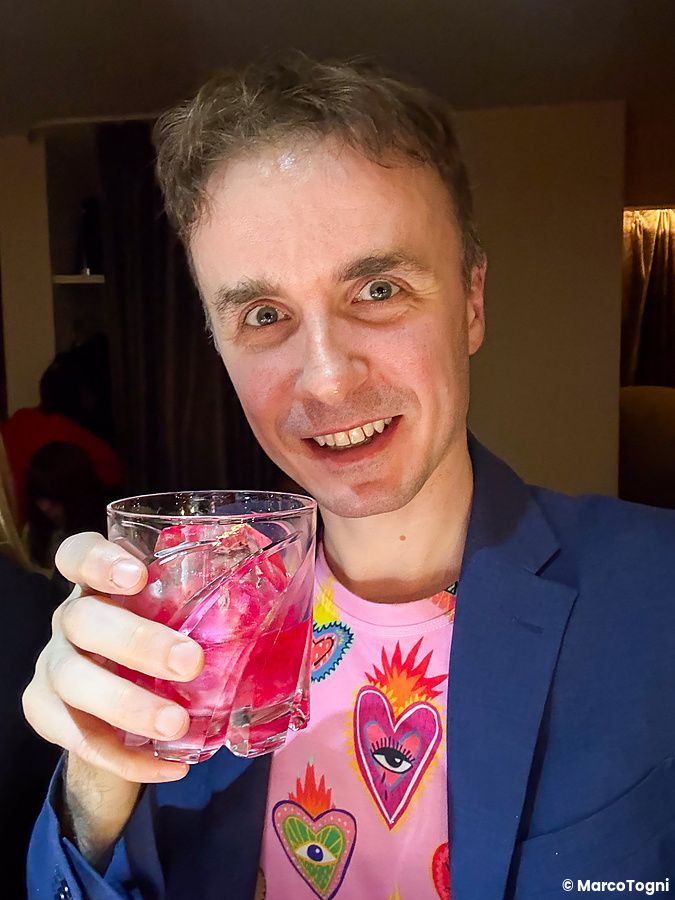 Marco Togni sorride tenendo un bicchiere con una bevanda rosa all'interno del Bar Centifolia a Tokyo.