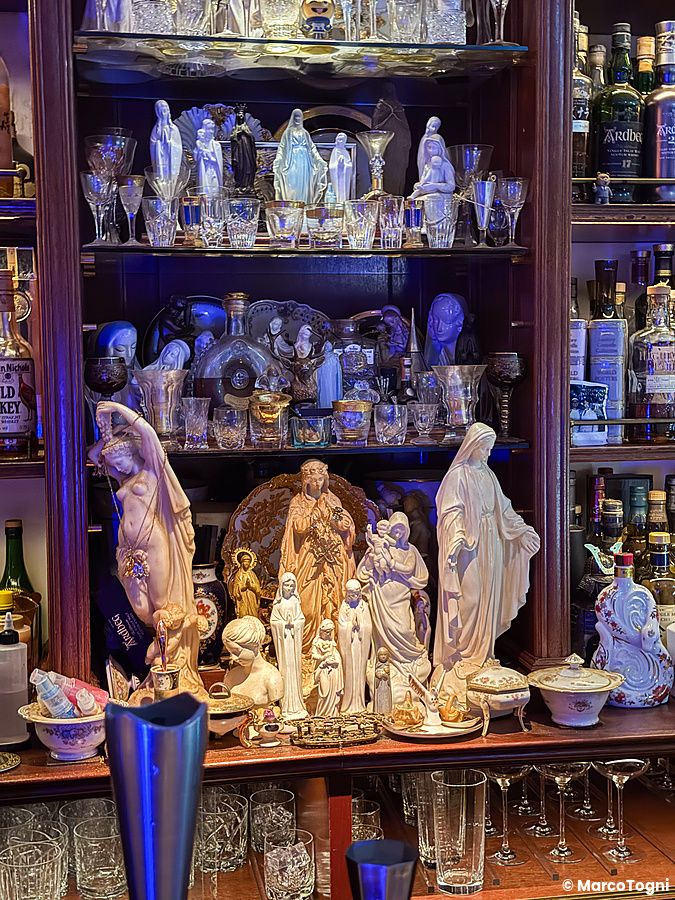 Una scaffalatura in legno del Bar Centifolia a Tokyo espone bottiglie di whisky, statuette religiose e oggetti in vetro.