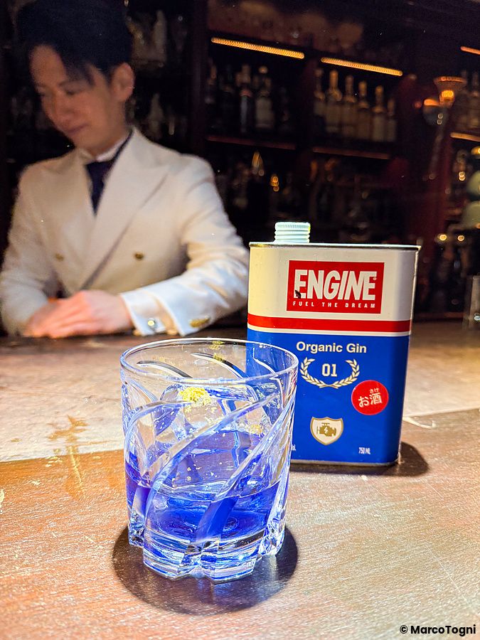 Un cocktail blu e una latta di Engine Gin sul bancone del Bar Centifolia a Tokyo con un bartender sullo sfondo.