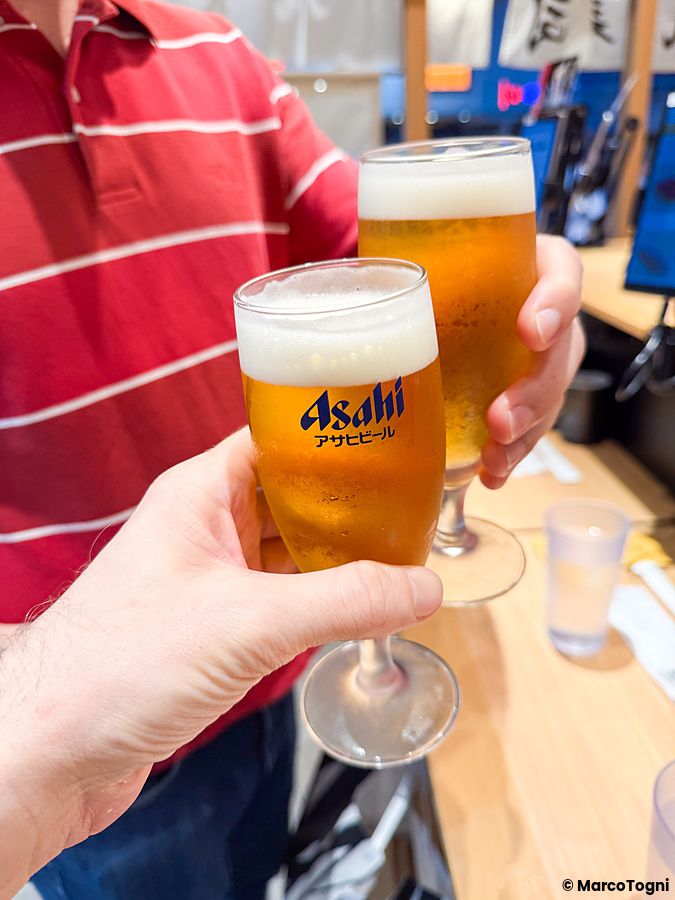 Due persone brindano con bicchieri di birra Asahi all'interno del ristorante Sushi Uogashinihonichi.