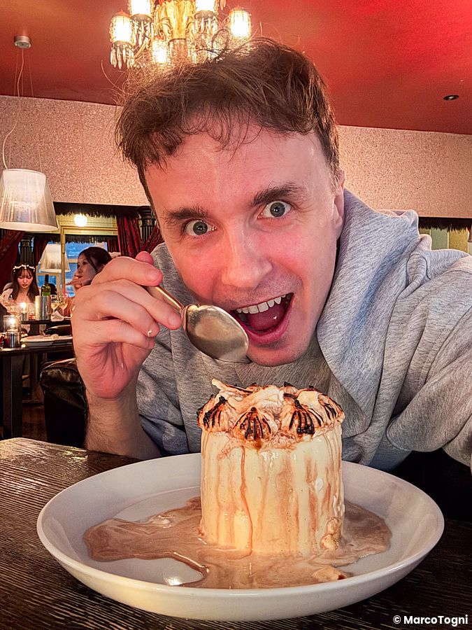 Marco Togni siede a un tavolo del Cafe Legato a Shibuya davanti a una torta Baked Alaska servita su un piatto bianco.