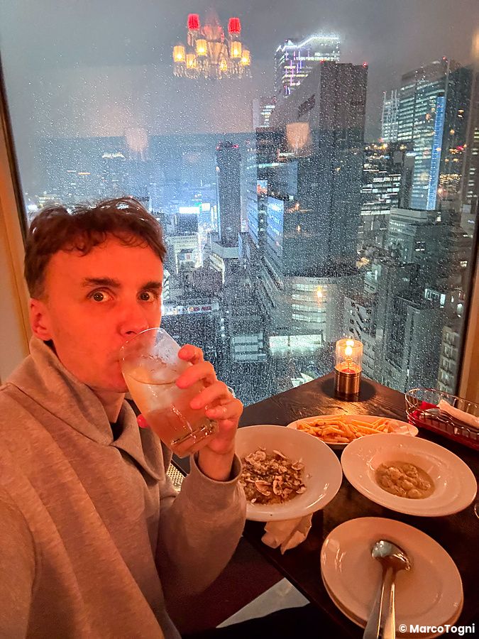 Marco Togni siede a un tavolo con risotto con funghi, gnocchi e un cocktail davanti alla vetrata del Cafe Legato a Shibuya.