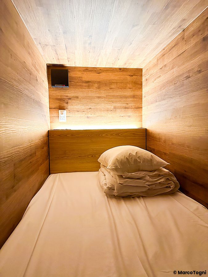 La capsula dove dormire a Rembrandt Cabin & Spa Shimbashi con rivestimenti in legno chiaro e letto preparato.