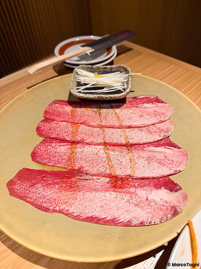 Fette di lingua di manzo cruda e pronta da cuocere a Ristorante Toraji disposte su un piatto rotondo con guarnizione.
