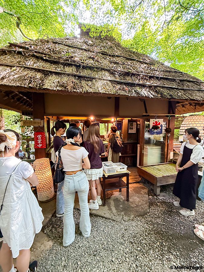 Persone in fila davanti al chiosco vicino al ristorante a Kurochaya, una struttura tradizionale in legno e paglia.