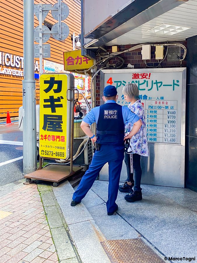 Un agente di polizia in uniforme parla con una persona in una strada del quartiere Kabukicho a Tokyo.