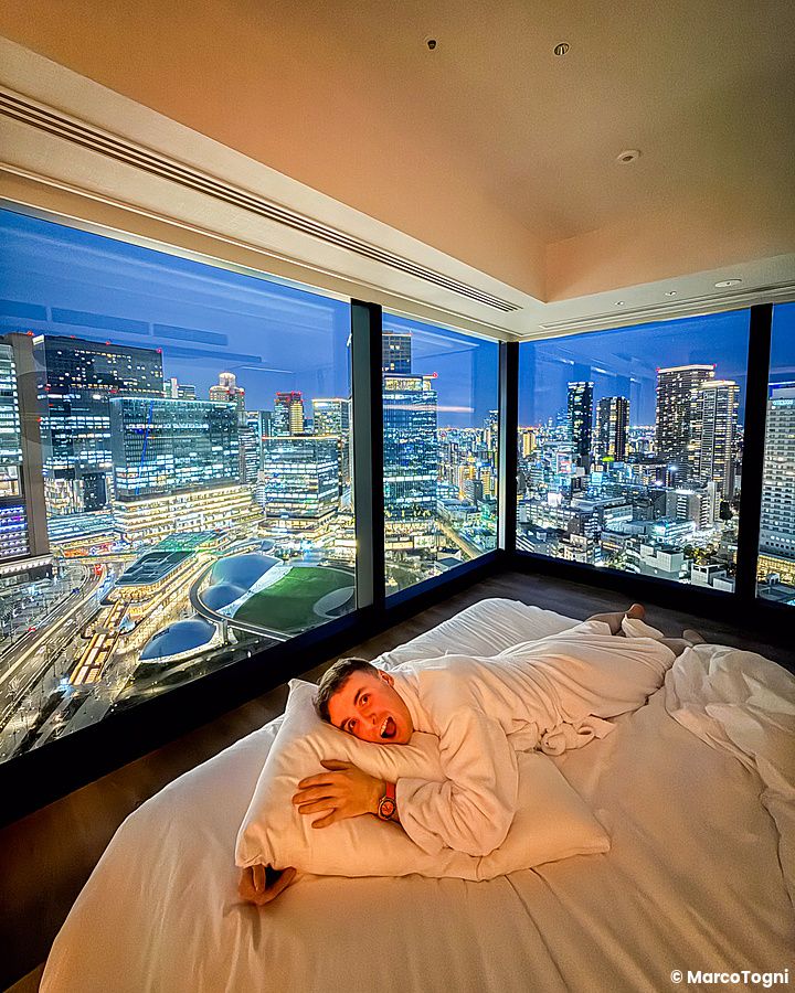 Marco Togni in accappatoio sdraiato sul letto in una corner room al Canopy by Hilton Osaka Umeda con vista su Umekita Park.