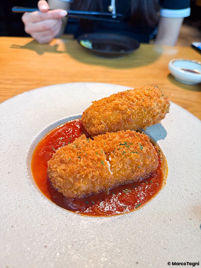 Due crocchette dorate su salsa di pomodoro servite in un piatto di ceramica al Kinka Sushi Bar Izakaya di Shibuya.