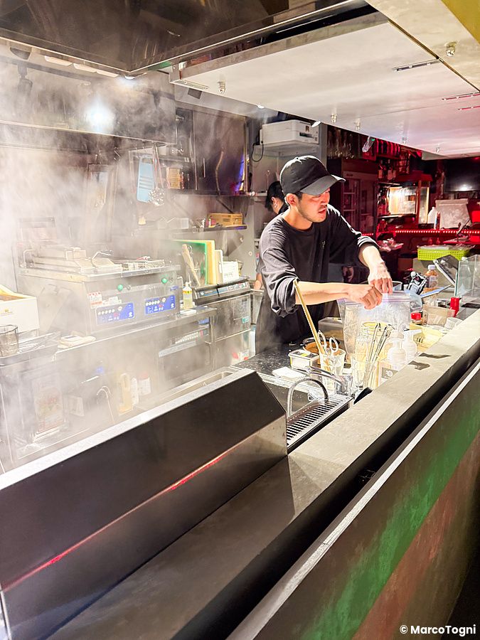Un uomo con cappellino lavora nella cucina del ristorante Neo Shinjuku Atsushi a Shinjuku tra vapori intensi.