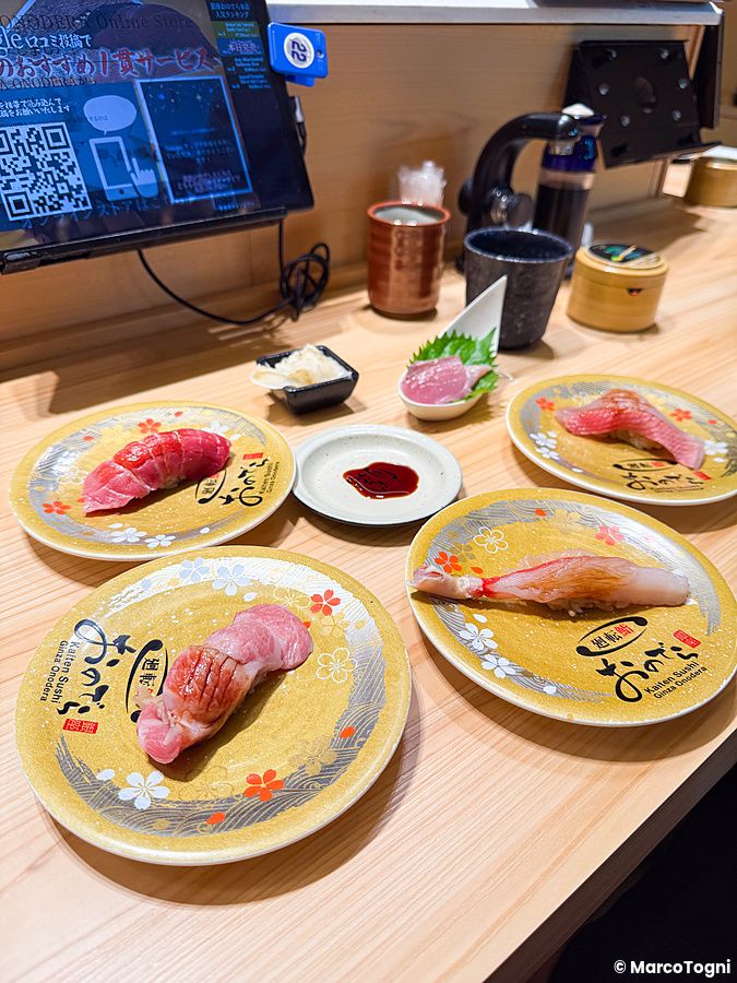 Piatti di sushi nigiri disposti su un bancone in legno all'interno del Kaiten Sushi Ginza Onodera a Omotesando.