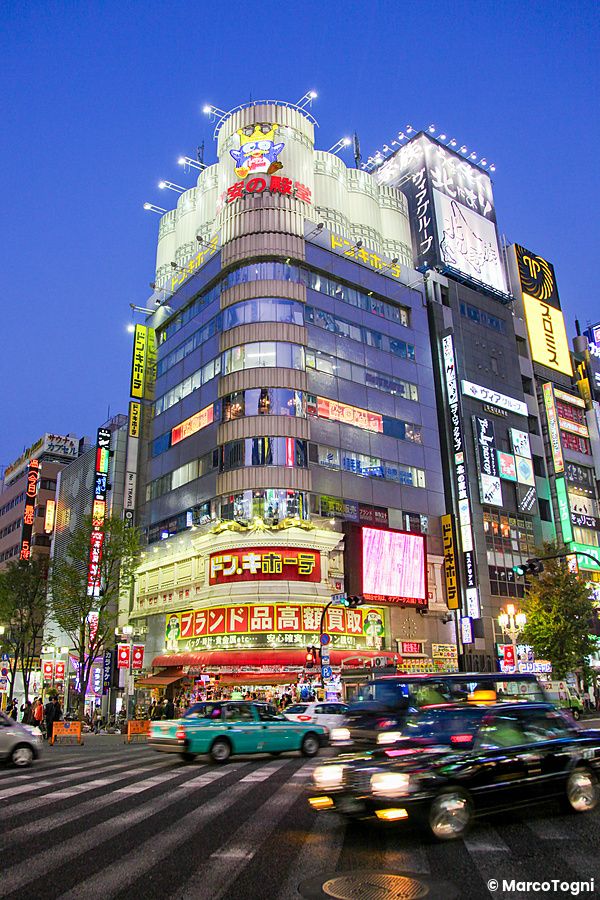 L'edificio del Don Quijote a Shinjuku con insegne luminose e traffico stradale in primo piano durante il crepuscolo.