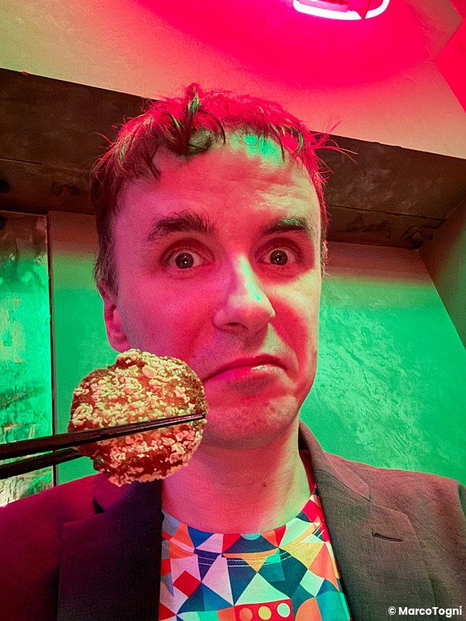 Marco Togni tiene un fungo fritto con le bacchette davanti al proprio viso all'interno del ristorante Neo Shinjuku Atsushi.