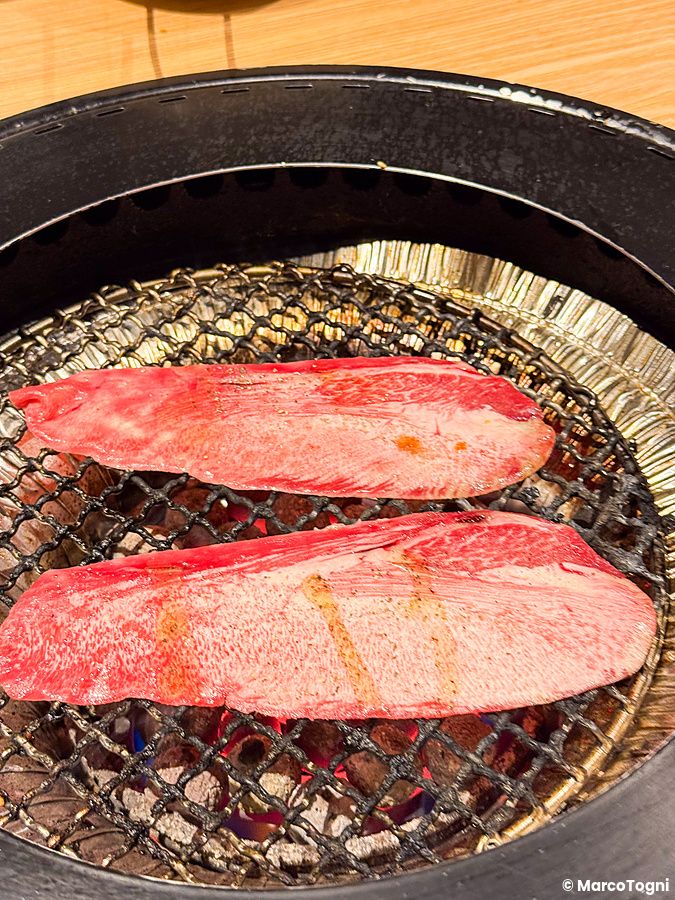Due fette di carne cruda disposte su una griglia circolare di metallo all'interno del Ristorante Toraji.