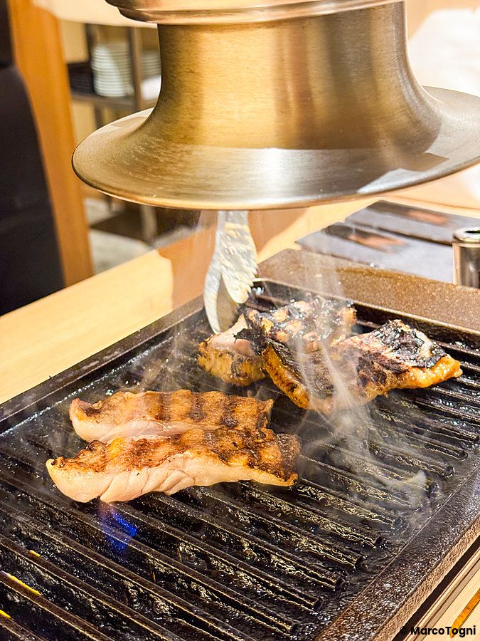 Pesce grigliato sulla piastra presso il ristorante Yakiuo Ishikawa a Roppongi, Tokyo, con vapore che sale verso la cappa.