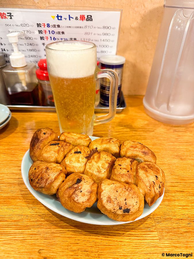 Un piatto di gyoza fritti e un boccale di birra chiara su un tavolo in legno al ristorante Fight Gyoza di Otsuka.