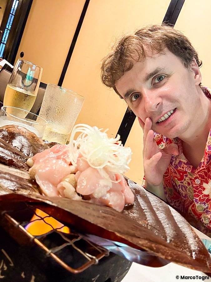 Marco Togni sorride accanto a un piatto di hobayaki con carne e miso servito presso il ristorante Kurochaya a Tokyo.