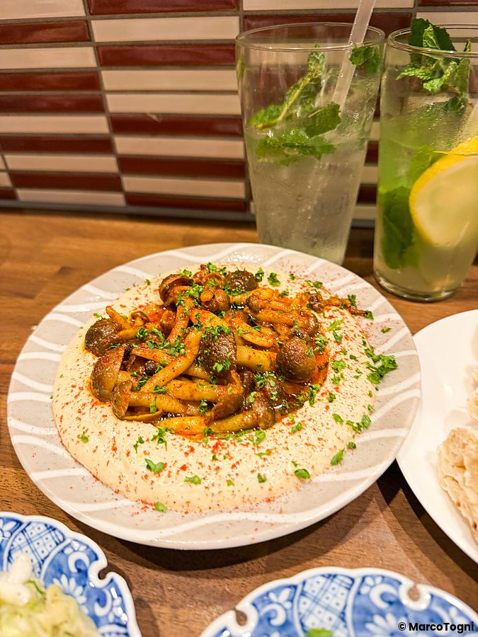 Un piatto di hummus con funghi saltati servito al ristorante Telaviv a Kyoto su un tavolo di legno.