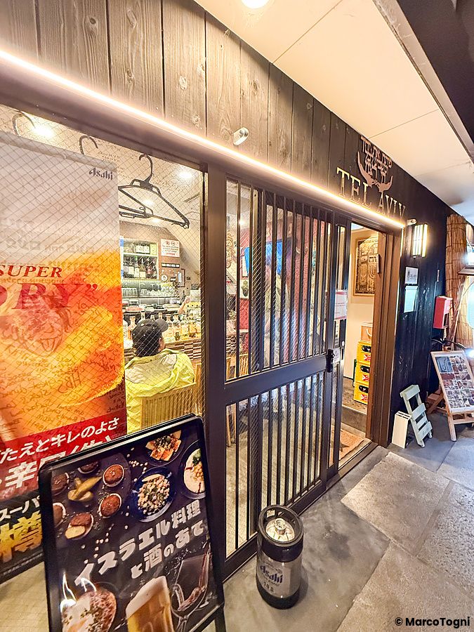 L'ingresso del Ristorante Telaviv a Kyoto con facciata in legno, una persona seduta all'interno e insegna con il nome.
