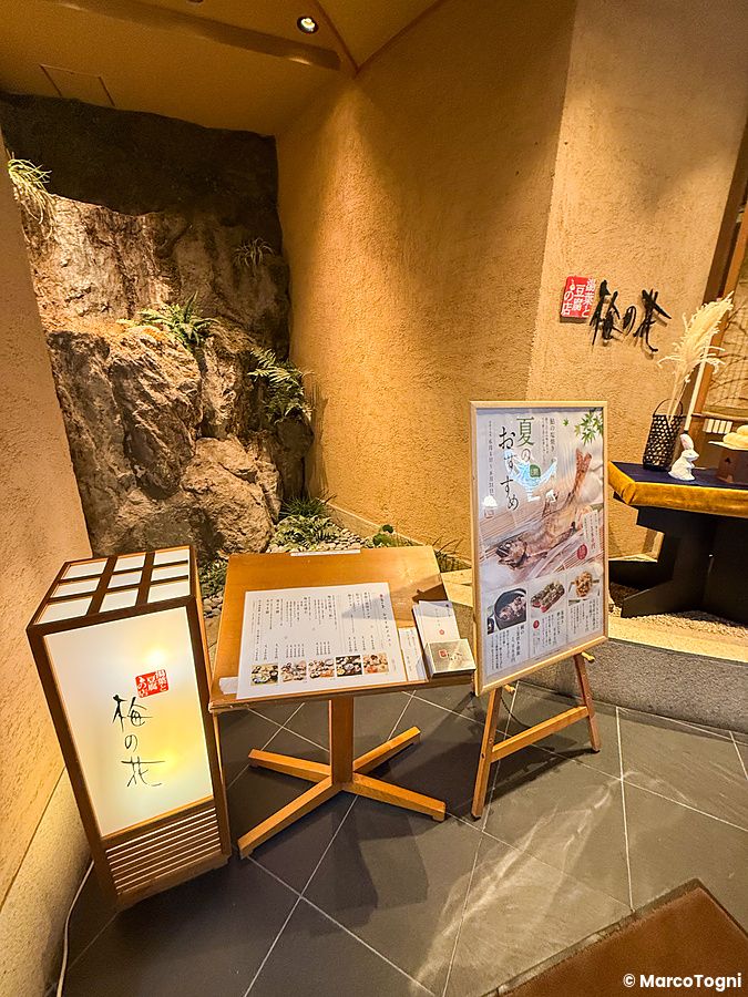 Ingresso a Ume no Hana a Ginza con leggio menu e lanterna illuminata accanto a una decorazione rocciosa.